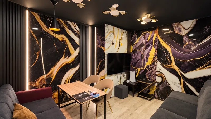 Private room with black and gold marble walls, sofas and a wall-mounted TV with PS5
